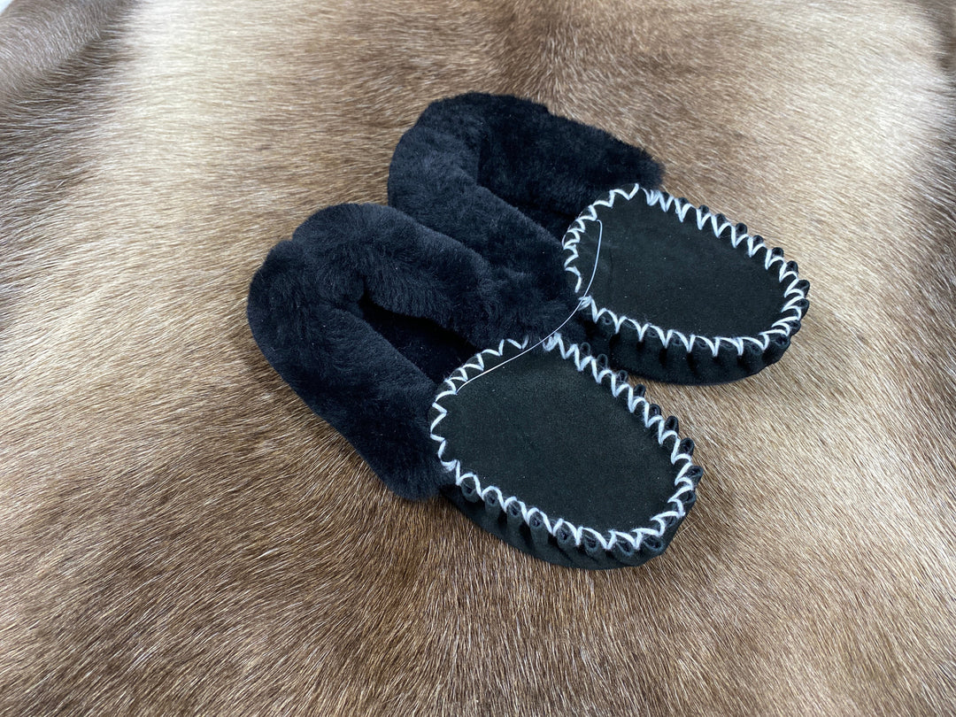 The Skin Thing black sheepskin moccasin slippers with white contrast stitching and fluffy lining.