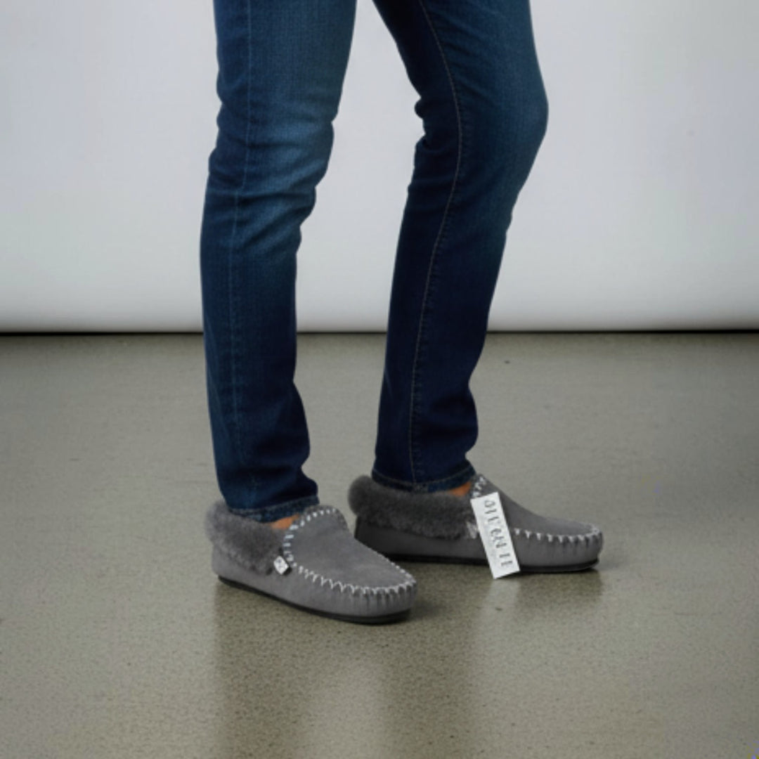 The Skin Thing grey sheepskin moccasins with white stitching and a fluffy trim, featuring an EVA sole.