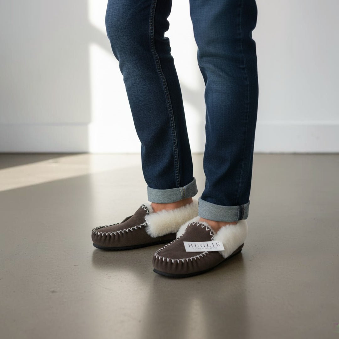 The Skin Thing HUGLIE brown sheepskin moccasin slippers with white fluffy lining and white stitching detail.