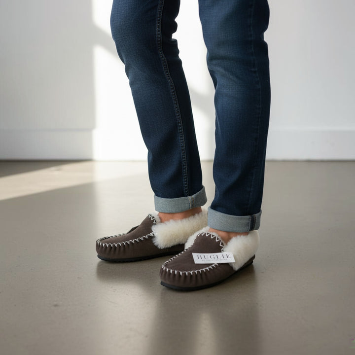The Skin Thing HUGLIE brown sheepskin moccasin slippers with white fluffy lining and white stitching detail.