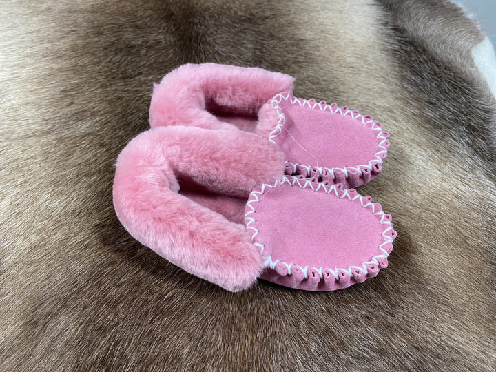 The Skin Thing pink sheepskin moccasin slippers with white stitching and a fluffy lining.